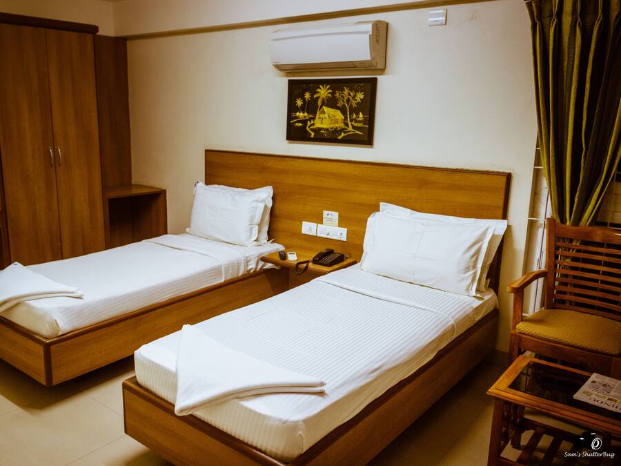 Two single beds with wooden frames and white linens, a wooden wardrobe, a bedside table with a phone, and a wall-mounted air conditioner.