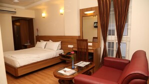 Une chambre d’hôtel avec un lit, une table de chevet en bois, un canapé en cuir rouge, une petite table en bois avec un magazine, et un miroir au-dessus du canapé.