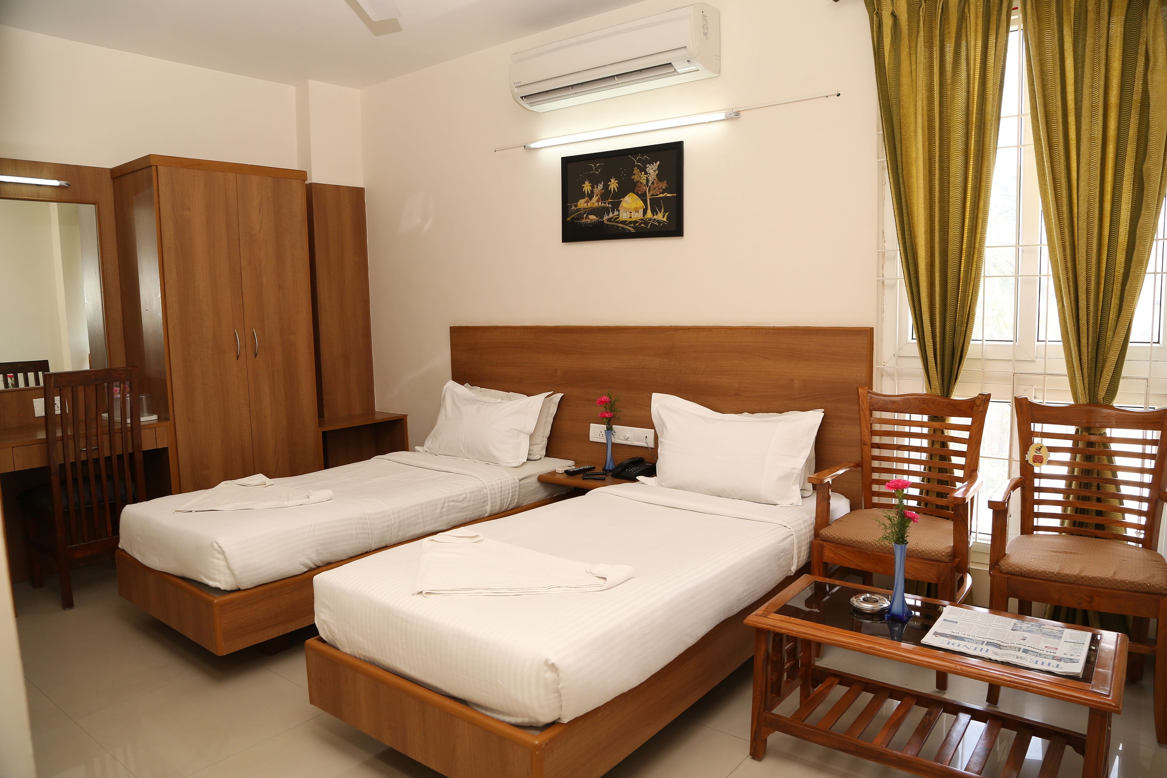 A hotel room with two single beds, wooden furniture, a desk, and a window with curtains.
