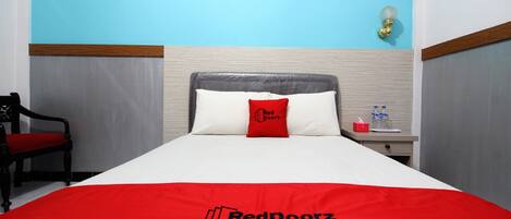 A hotel room with a bed, a nightstand, a chair, and a wall-mounted lamp.