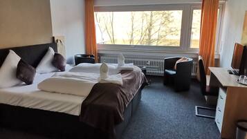A hotel room with a bed, a desk, a chair, and a view of trees through the window.