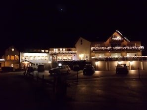 Een hotel met meerdere verdiepingen, balkons met verlichting en auto's op de oprit.