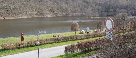 A riverside pathway with a sculpture, directional signs, and a no-entry sign.