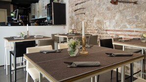 A restaurant interior with tables set for dining, a brick wall, and a mounted fish hook decoration. - Heritage Hotel Cardo (Split)