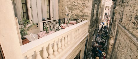 A narrow street with a balcony overlooking a crowded area.