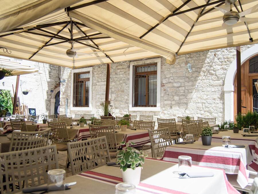 Un café al aire libre con paredes de piedra, muebles de madera y plantas colgantes.