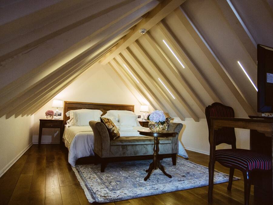 A cozy bedroom with a bed, a nightstand, a table with a vase, and a chair.