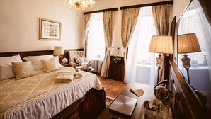 A hotel room with a large bed, a desk with a laptop, a chair, a lamp, a mirror, and a chandelier. - Heritage Hotel Cardo (Split)