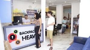 Una zona de recepció amb un cartell que diu "BACKPACKERS HEAVEN" i un cartell de "TRAVEL LOUNGE" al fons.