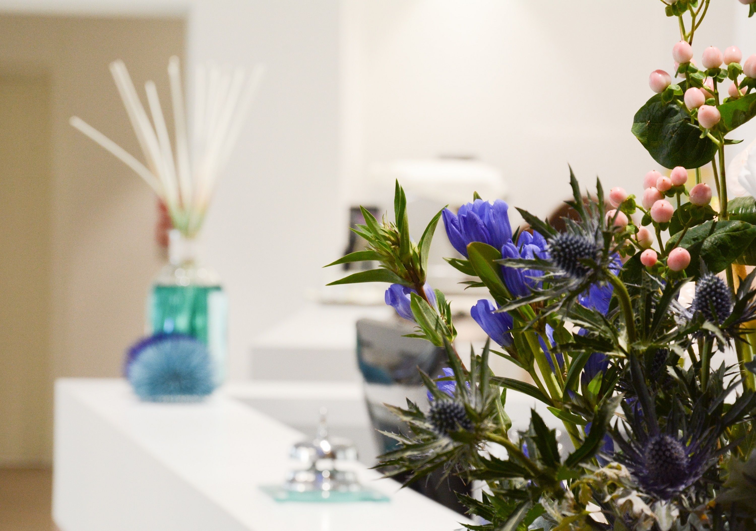Un mostrador de recepción con un florero, un dispensador de gel hidroalcohólico y un pequeño objeto decorativo.