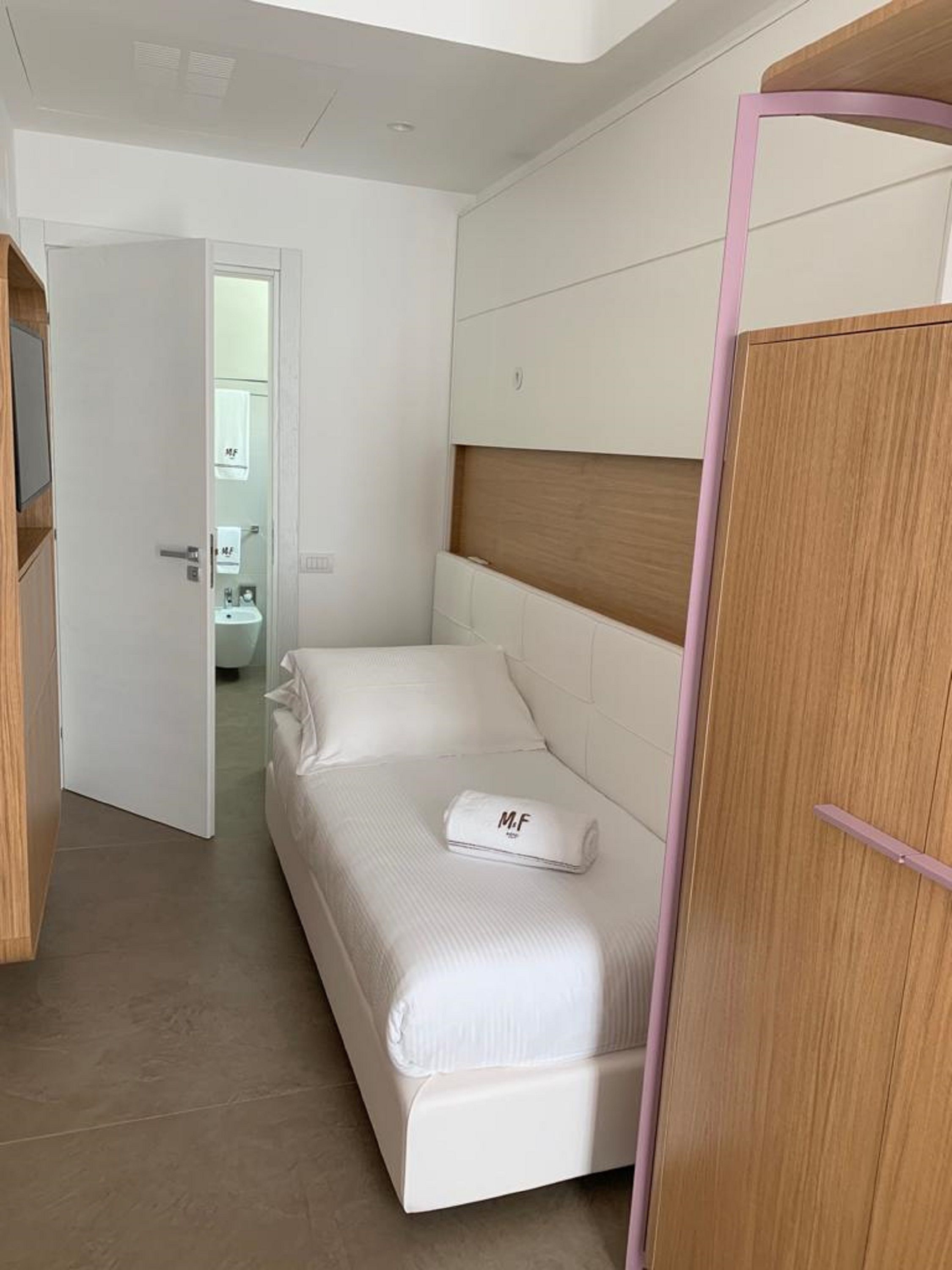 A modern bedroom with a large bed, a wooden wardrobe, and a bathroom visible through an open door.