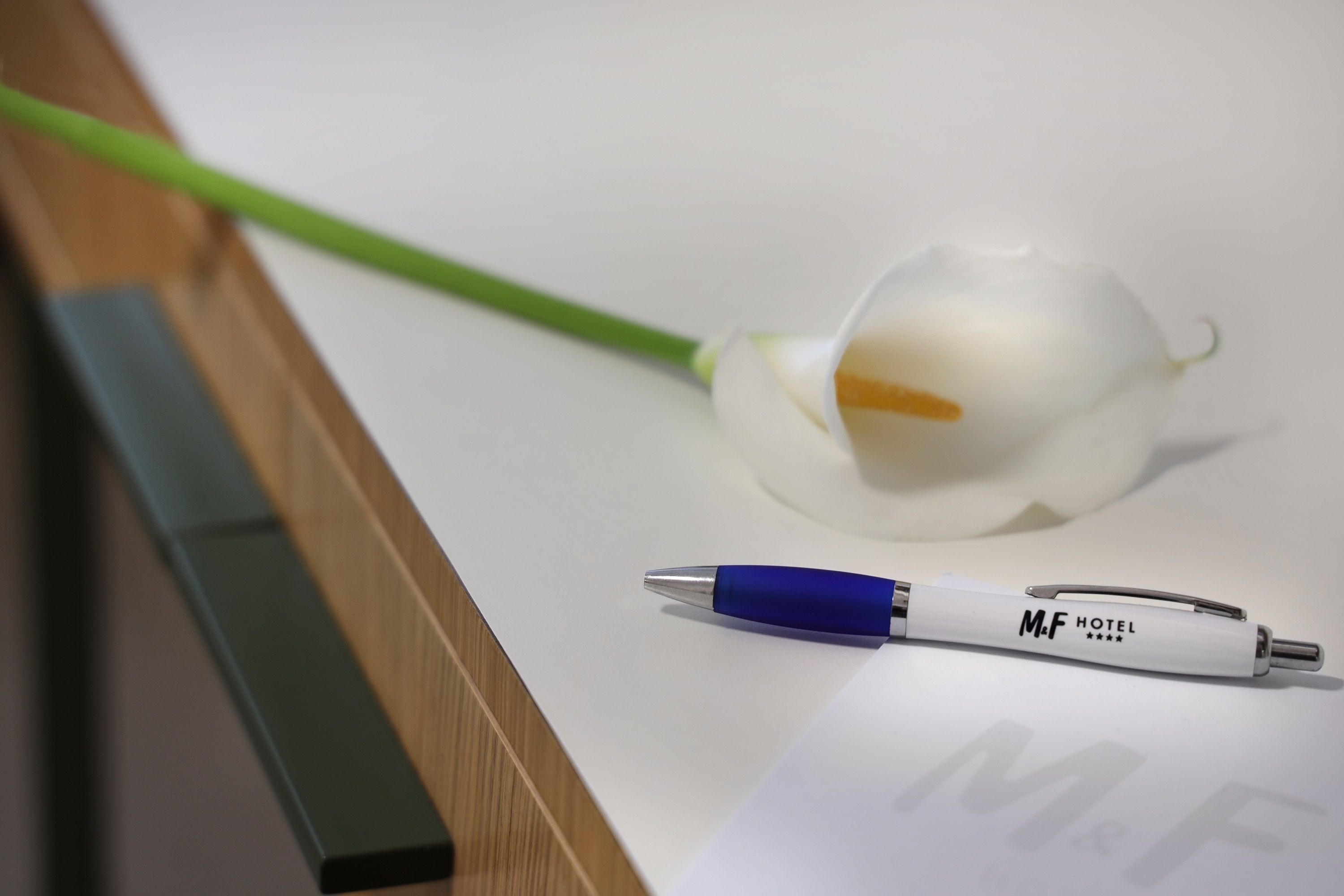 Una penna bianca con la scritta "M.F HOTEL" e un fiore bianco su una superficie bianca.