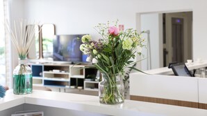 A modern hotel lobby with a reception desk, a television, and a vase of flowers on the counter. - M&F Hotel (Gallipoli)