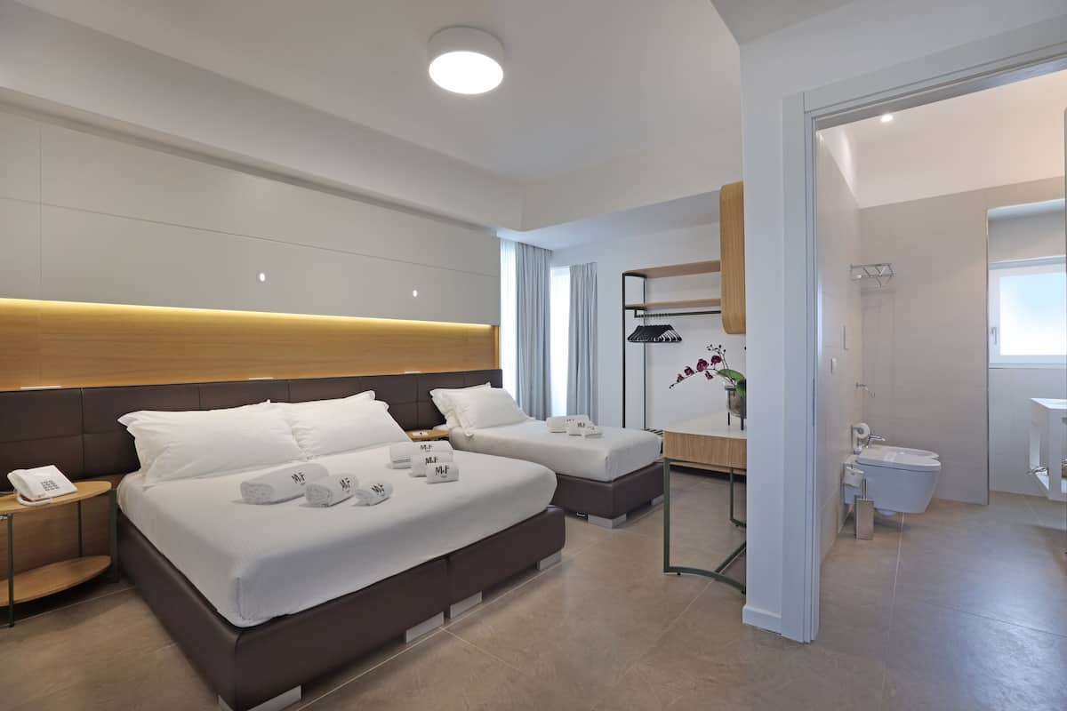 Una habitación de hotel moderna con una cama grande, dos mesitas de noche, un tocador, un espejo, un escritorio pequeño y un baño con inodoro y lavabo.
