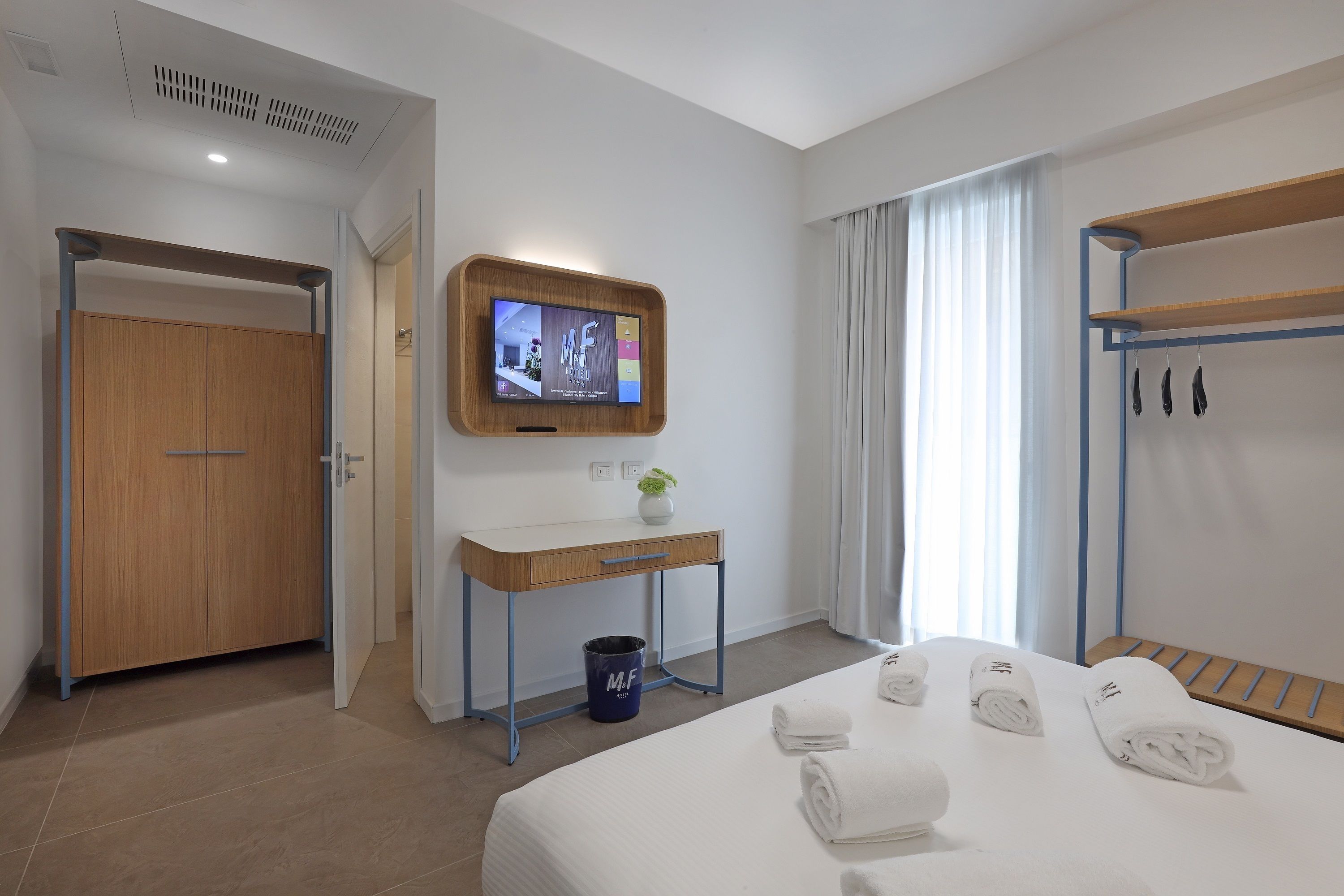 Une chambre d’hôtel avec un lit, un bureau, une télévision, un porte-manteau et une porte de salle de bain.