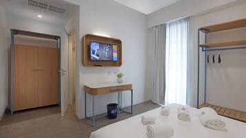Une chambre d’hôtel avec un lit, un bureau, une télévision, un porte-manteau et une porte de salle de bain.