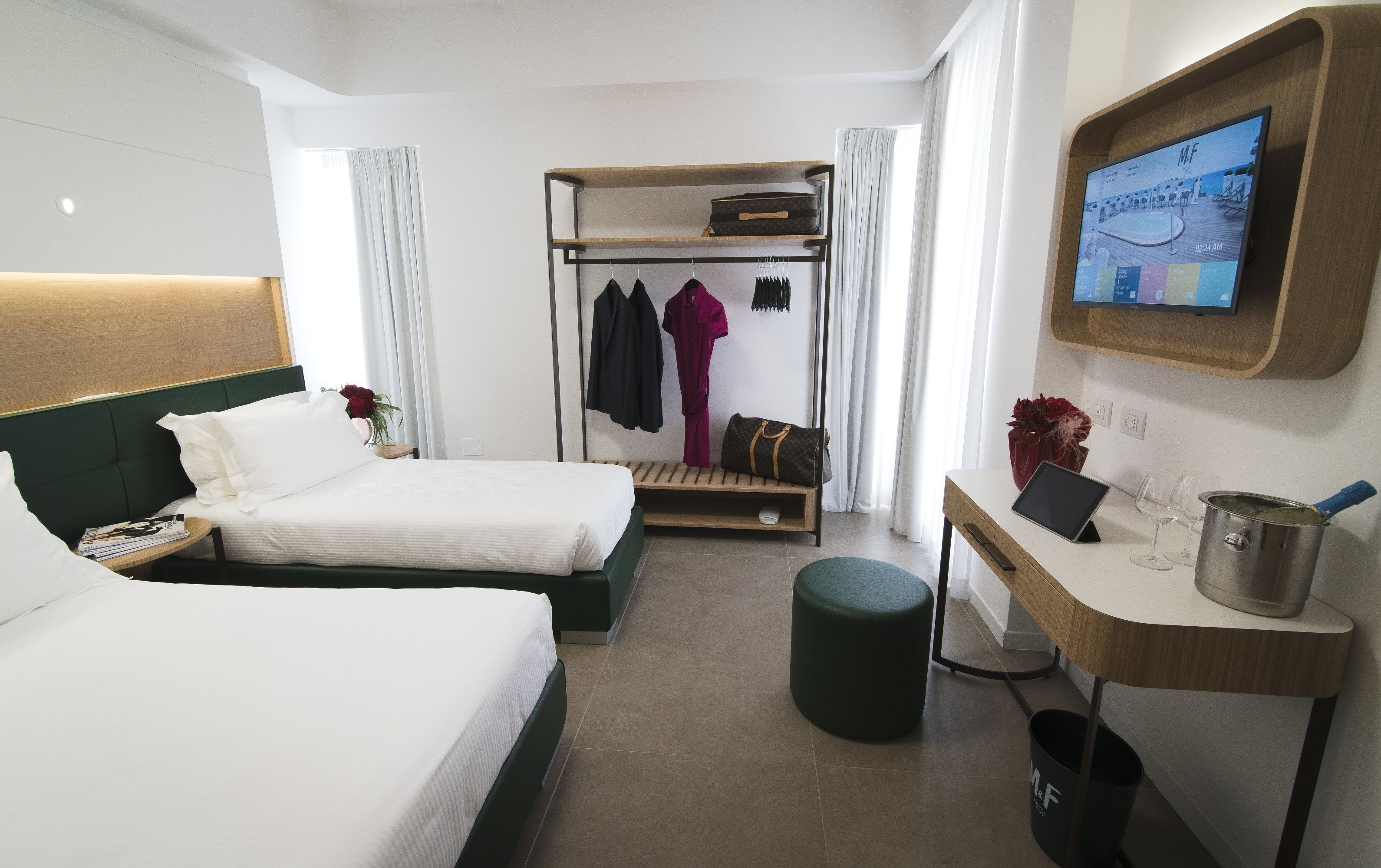 A hotel room with two beds, a desk, a TV, and a coat rack.