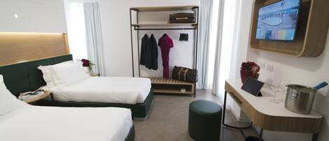 A hotel room with two beds, a desk, a TV, and a coat rack.