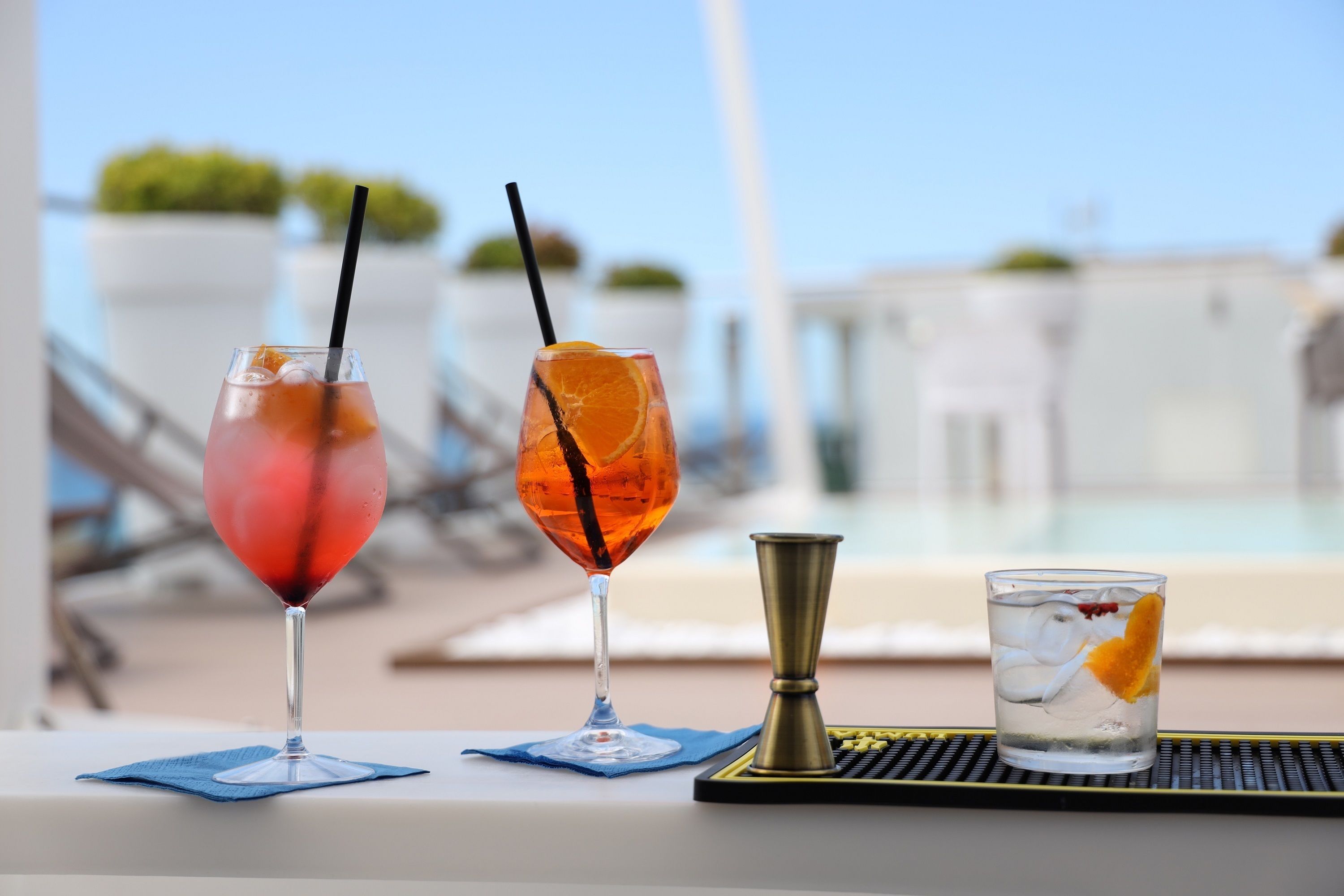 Two cocktails on a table near a poolside area with lounge chairs and a clear view of the pool.