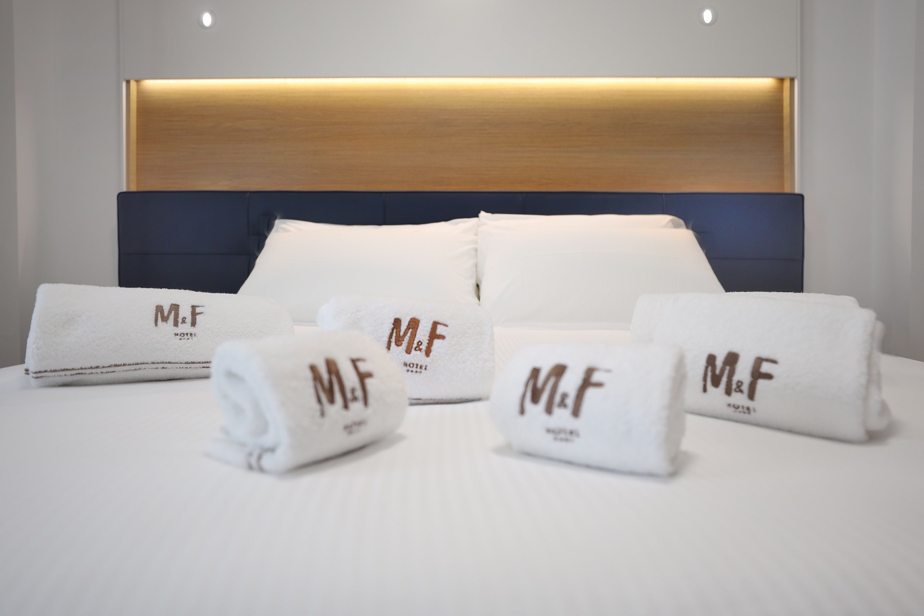Un lit bien fait, avec du linge de lit blanc et des oreillers, ainsi que quatre serviettes pliées, chacune ornée des initiales « M et F ».