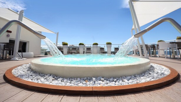 A circular hot tub with water jets on a wooden deck, surrounded by white pebbles and a wooden border. - M&F Hotel (Gallipoli)