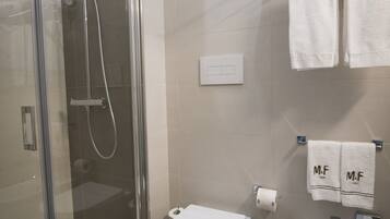 A modern bathroom with a glass-enclosed shower, a toilet, and a bidet.