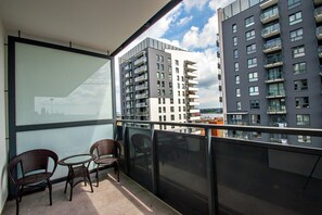 Un balcon avec deux fauteuils en osier et une petite table, d’où l’on peut admirer un paysage urbain avec des bâtiments modernes.