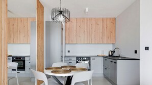 A modern kitchen with white cabinetry, a central island with a round table and chairs, and a unique pendant light. - Grand Apartments - Bastion Wałowa (Gdansk)