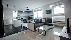 A modern living room with a sectional sofa, a glass coffee table, and a dining area with a view. - Grand Apartments - Bastion Wałowa (Gdansk)