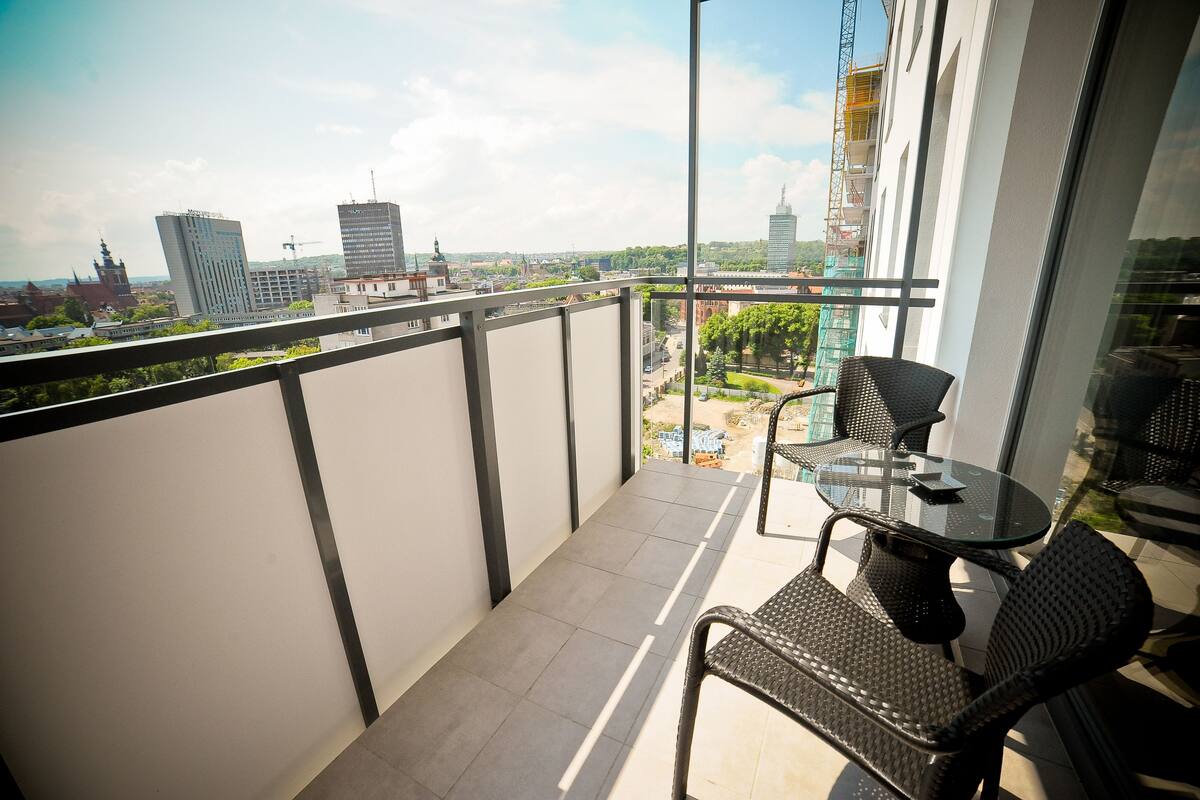 Un balcon doté d’une balustrade en verre, de deux fauteuils en osier et d’une petite table ronde.