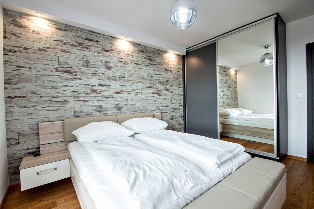 Une chambre moderne avec un mur en bois, un lit avec une literie blanche, une table de chevet et un grand miroir.