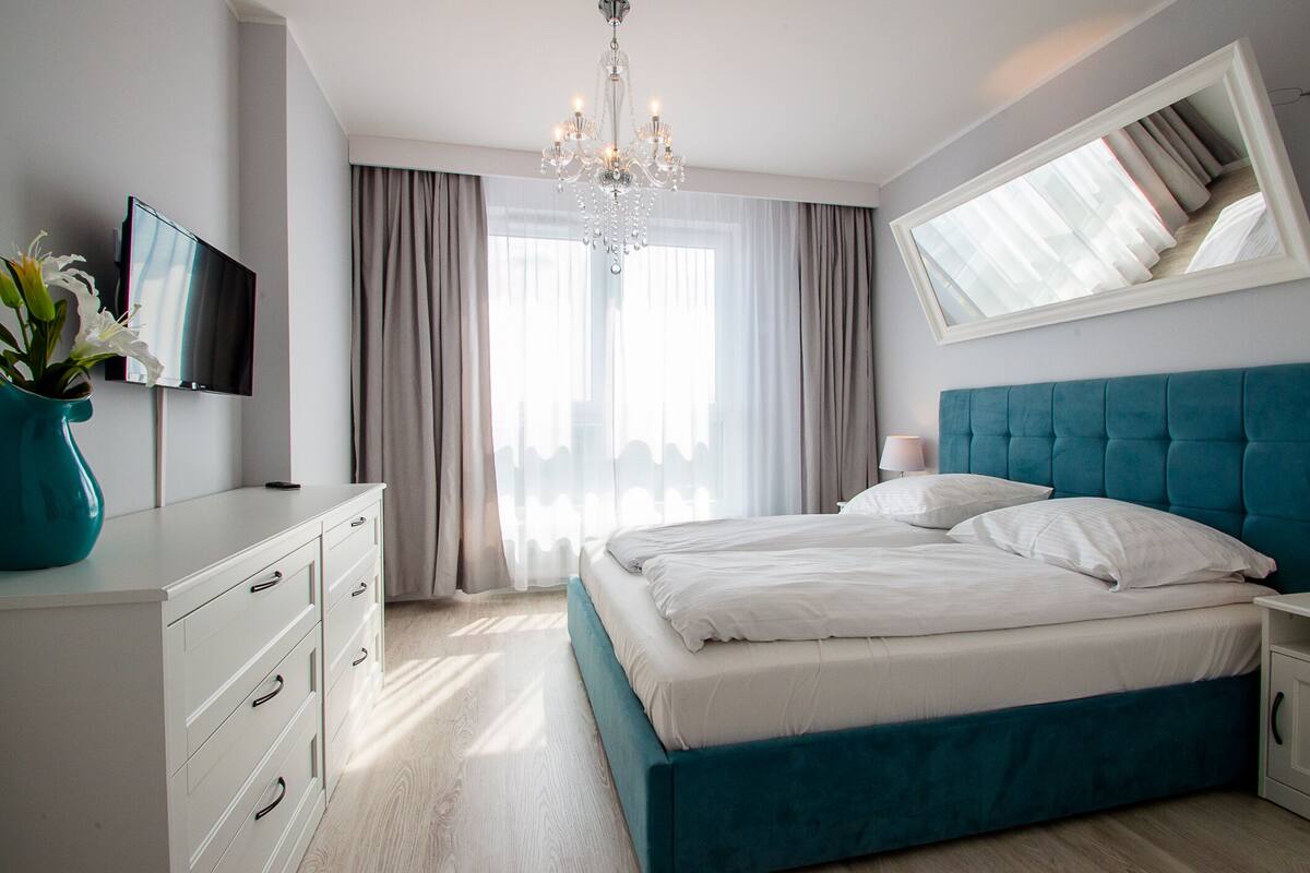 Une chambre à coucher moderne avec un lit, une télévision, une commode et un lustre.