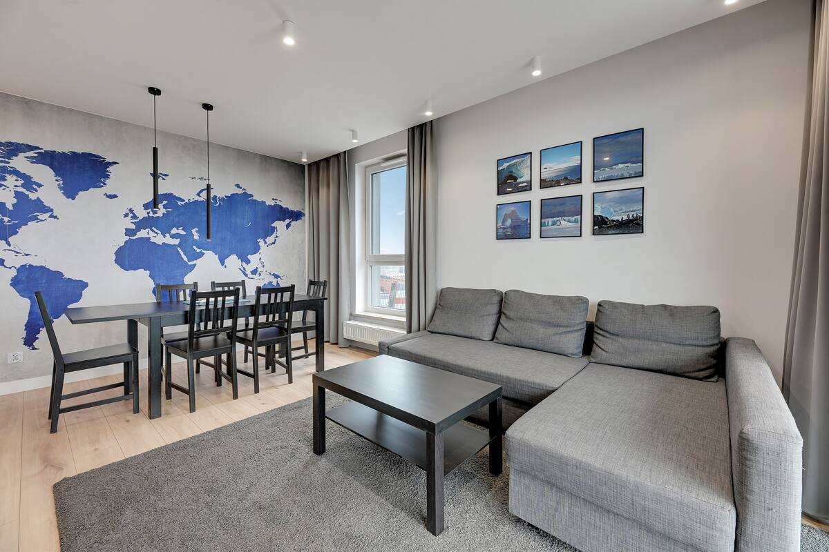 Un salon moderne avec un canapé gris, une table à manger avec des chaises, une table basse et une carte du monde accrochée au mur.