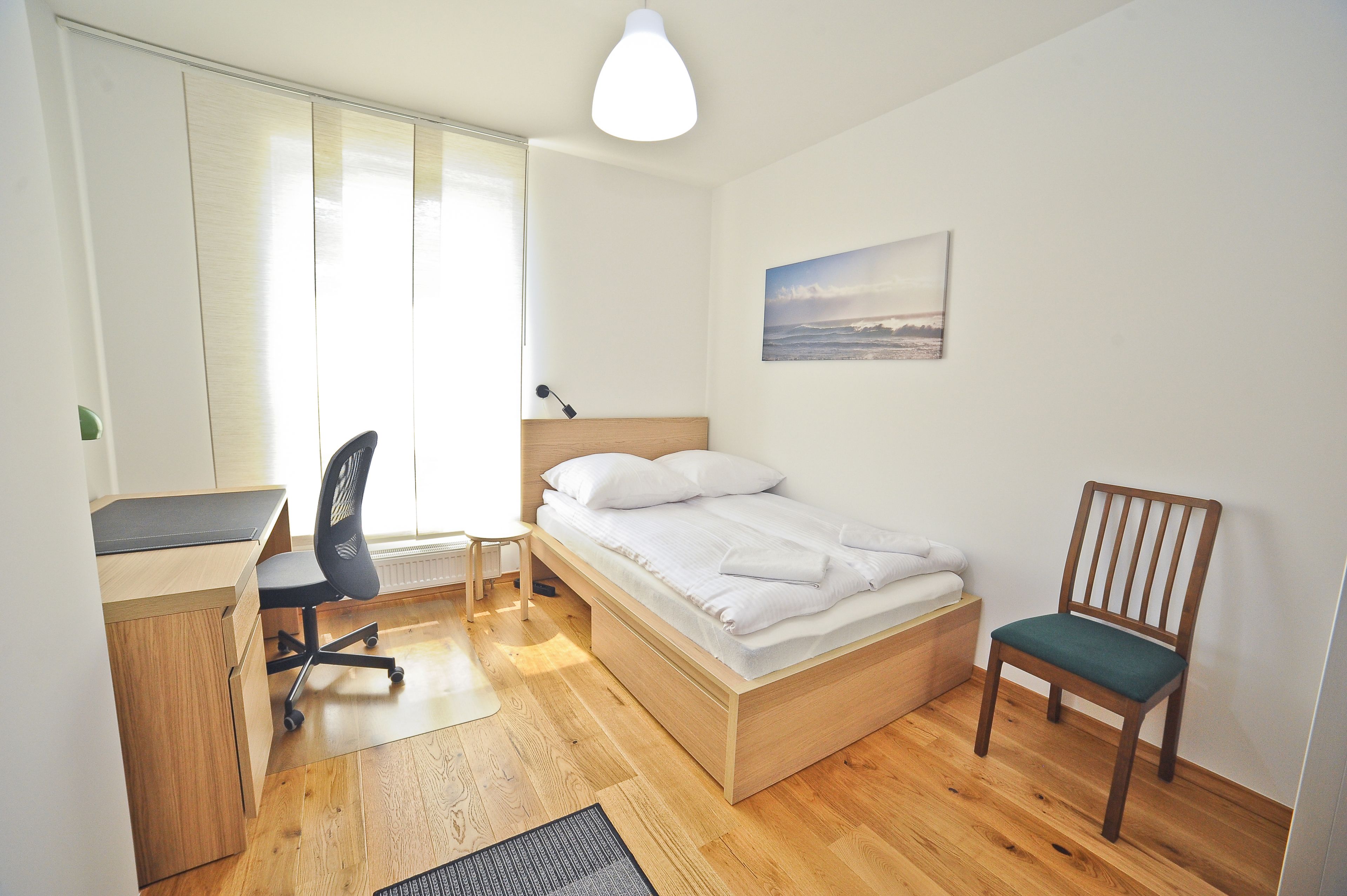 Ein Schlafzimmer mit einem Bett, einem Schreibtisch, einem Stuhl und einem Fenster.