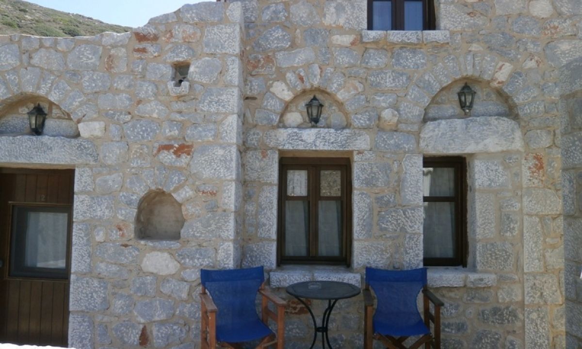 A stone building with arched windows and doors, a small table, and blue chairs.