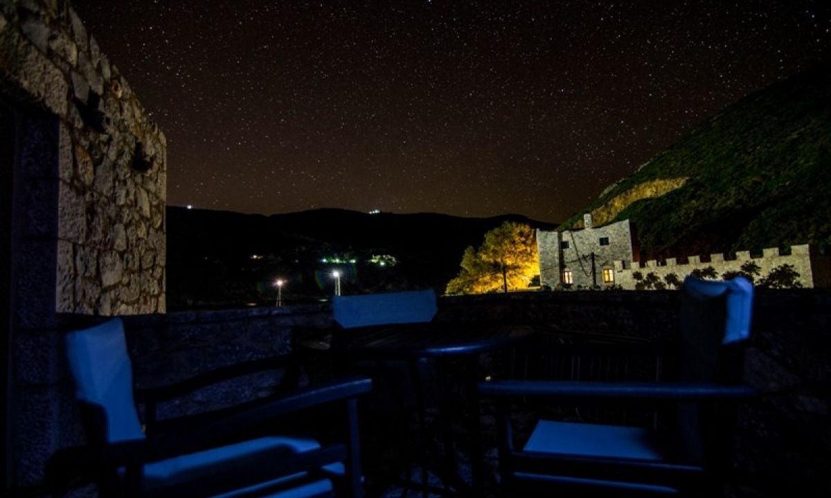 An outdoor seating area with stone walls and a view of a hill with a building.