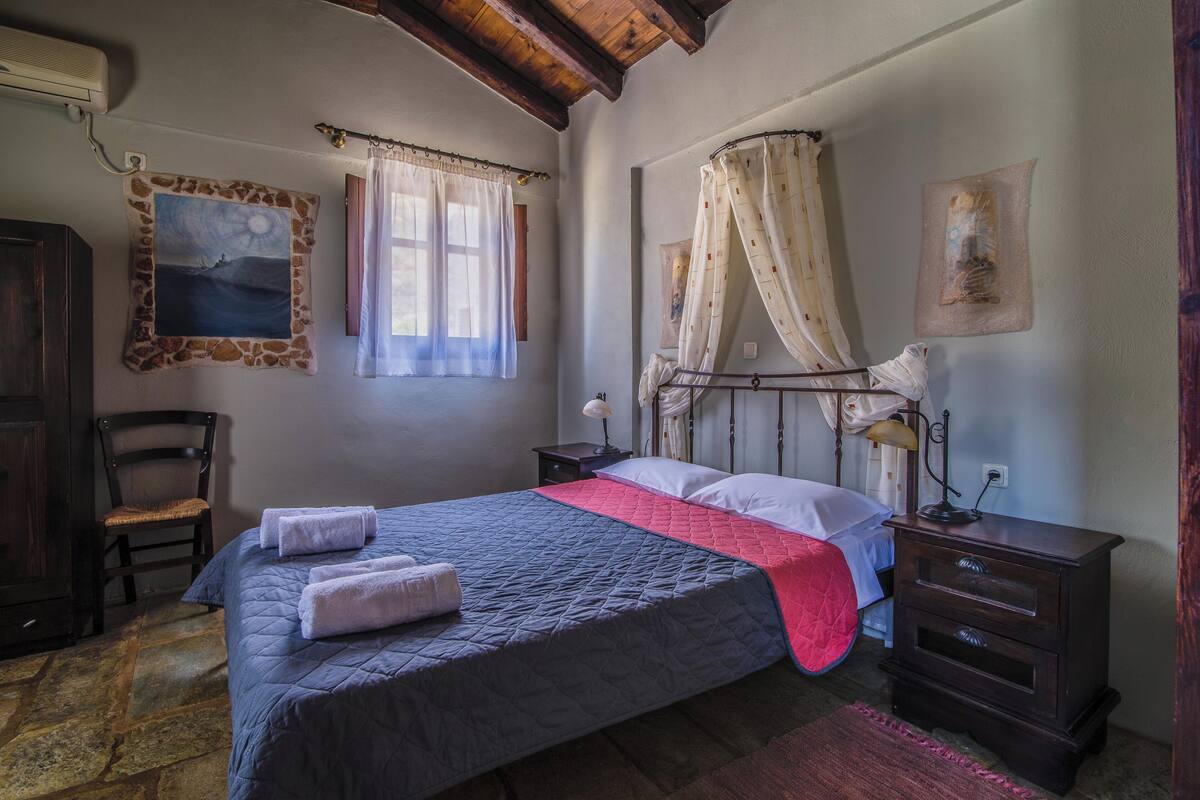 A bedroom with a bed, a chair, a nightstand, a lamp, and a painting on the wall.