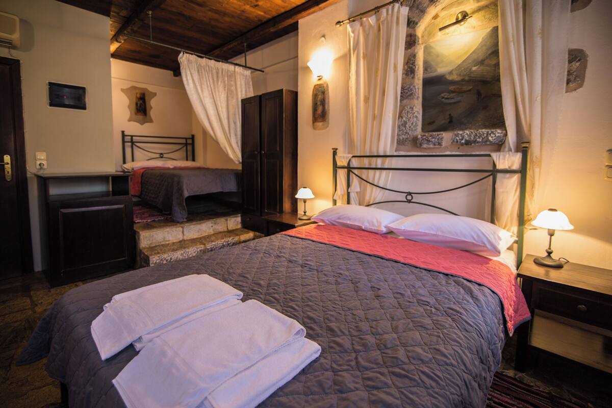 A bedroom with a large bed, two bedside tables, a nightstand, a wardrobe, and a window with curtains.