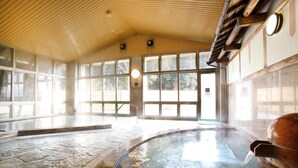 Una grande piscina interna con pavimento in pietra, soffitto in legno e ampie finestre che lasciano entrare la luce naturale.