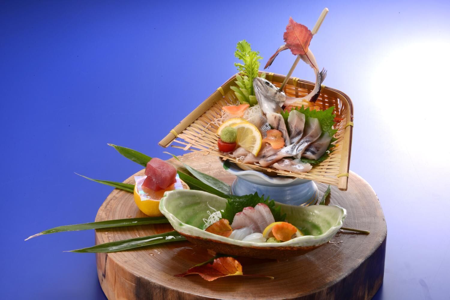 A wooden table with a woven basket containing various seafood items, a bowl with sashimi, and a decorative leaf.