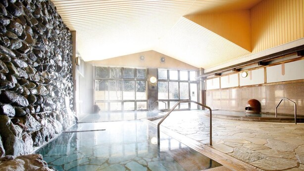 Una piscina interna con pareti in pietra, acqua cristallina, un solarium in legno e una zona sauna.