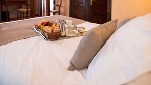 Cama bem arrumada com uma bandeja de itens de café da manhã, um jarro e uma xícara, em um quarto com porta de madeira e parede de pedra.
