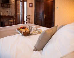 Cama bem arrumada com uma bandeja de itens de café da manhã, um jarro e uma xícara, em um quarto com porta de madeira e parede de pedra.