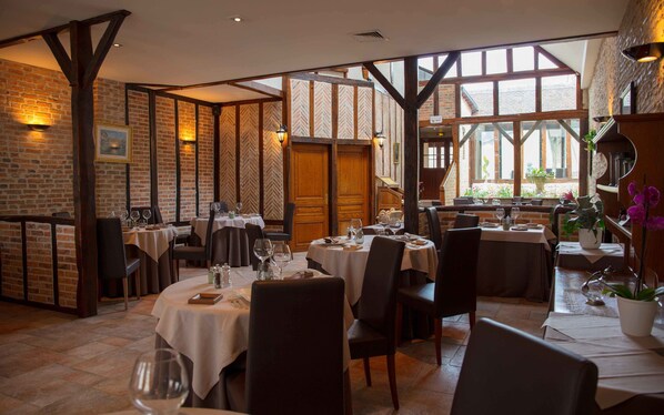 A restaurant with brick walls, wooden beams, and large windows. Tables are set with white tablecloths and chairs. - La Chaumière (Aubigny-sur-Nere)