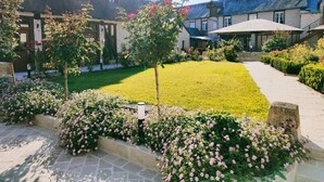 Um jardim bem cuidado com gramado, canteiros de flores e um caminho que leva a um edifício com telhado inclinado.
