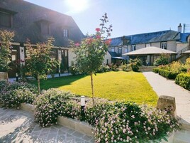 Um jardim bem cuidado com gramado, canteiros de flores e um caminho que leva a um edifício com telhado inclinado.