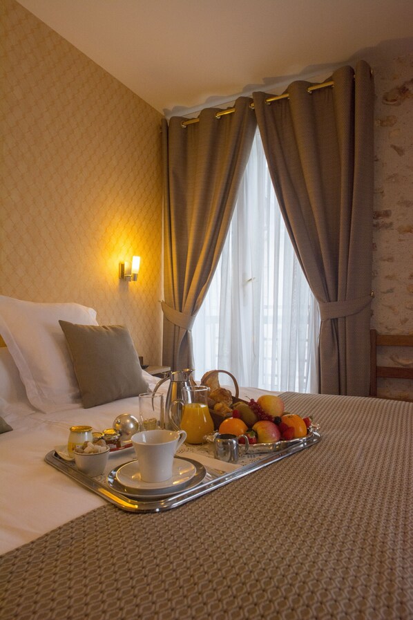 A hotel room with a neatly made bed, a tray with breakfast items, and a window with curtains.