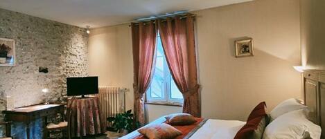 Un dormitorio con cama, escritorio, televisión y ventana con cortinas.