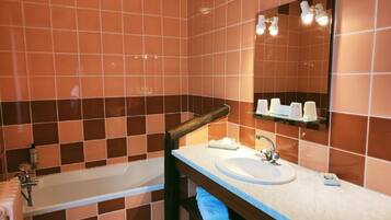 Un baño con bañera, lavabo, espejo y estante con artículos de aseo.
