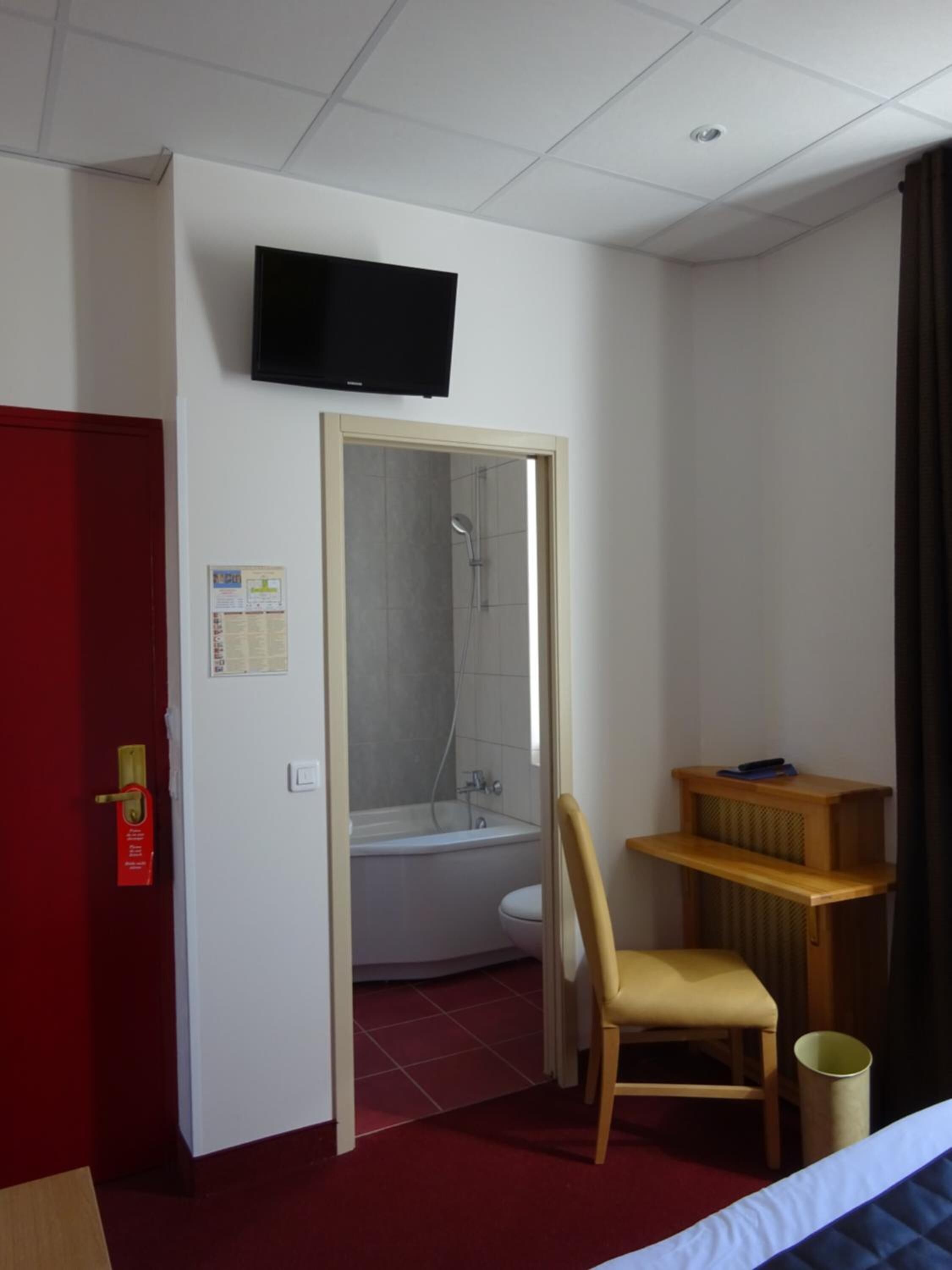 Habitación de hotel con ducha, inodoro y televisor instalado en la pared.